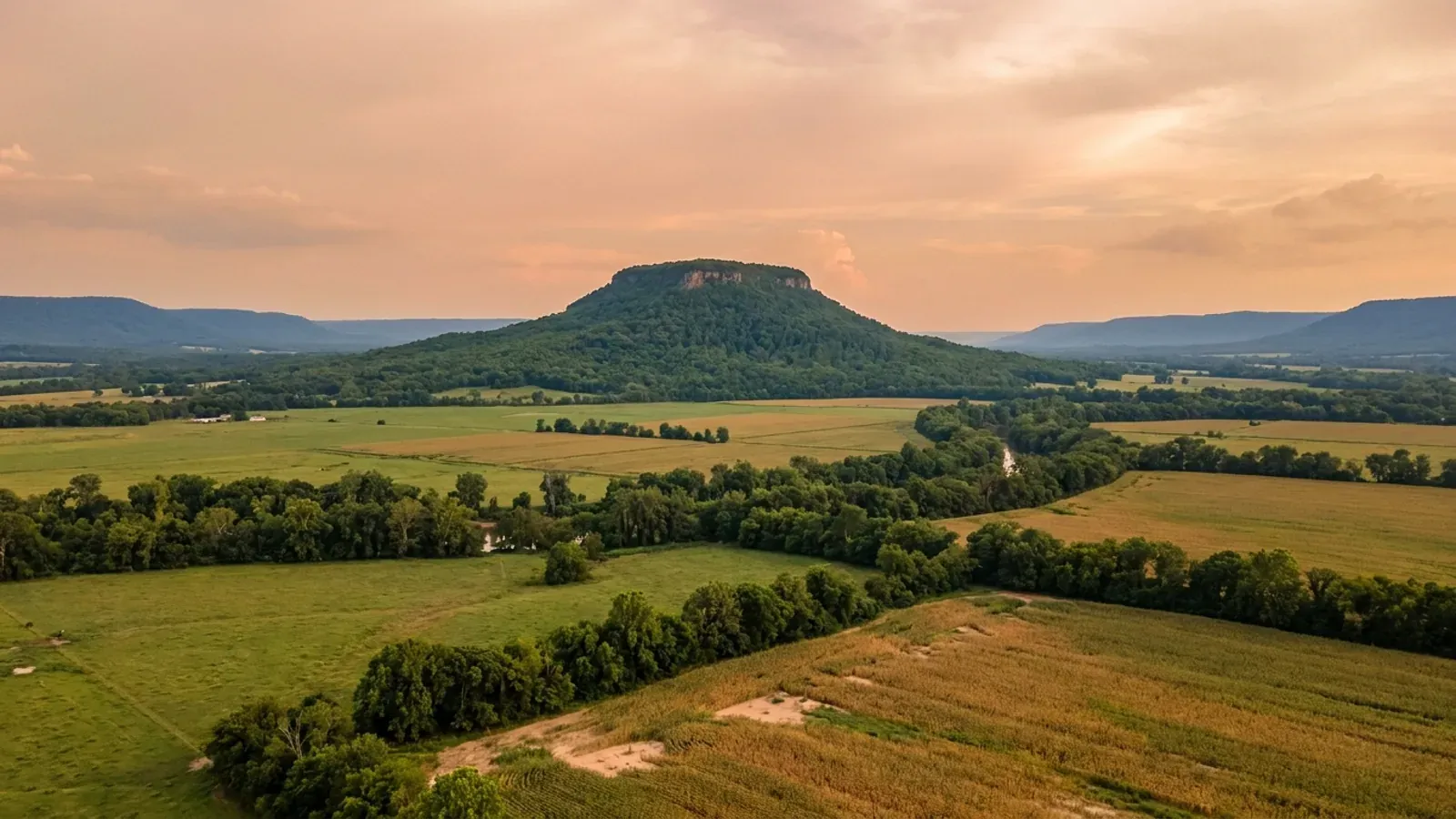 A broad flat river valley in pasture and crop with a flat-topped mountain rising abruptly behind it.