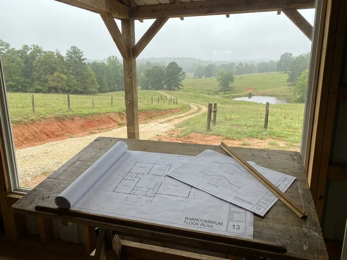 Barndominium floor plan and elevation drawings laid out on a drafting table with a scale rule.