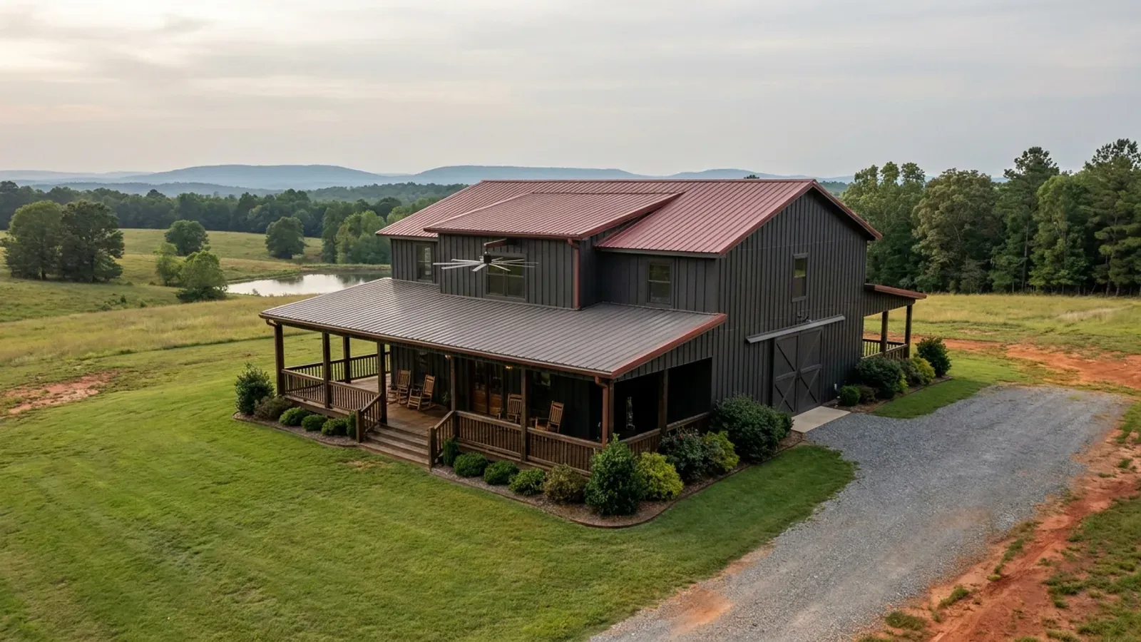 A barndominium exterior showing a deep wrap-around covered porch with posts and railing along two sides of the building.