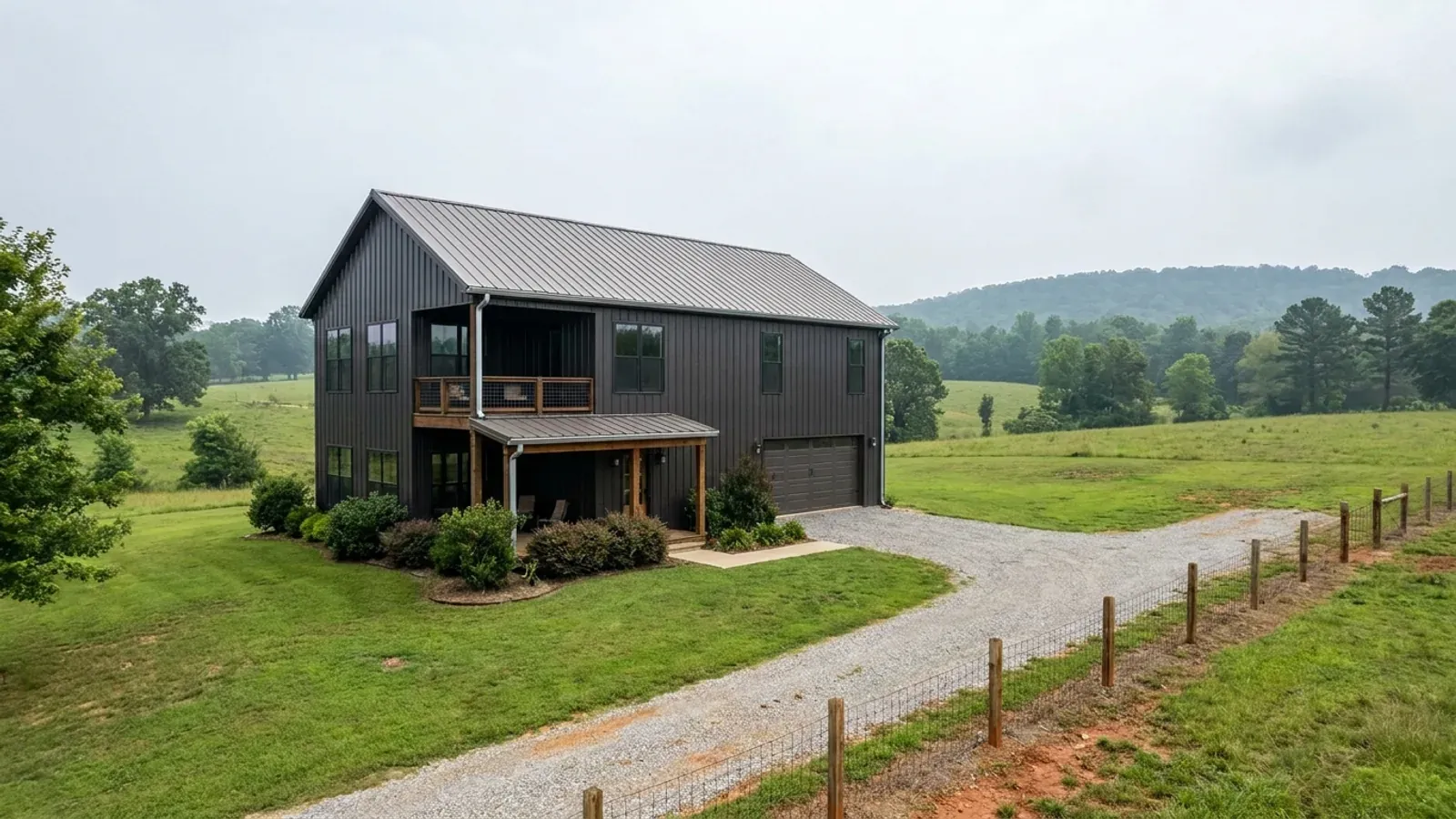 A completed two-story barndominium with visible second-story windows and a small covered balcony above the entry porch.